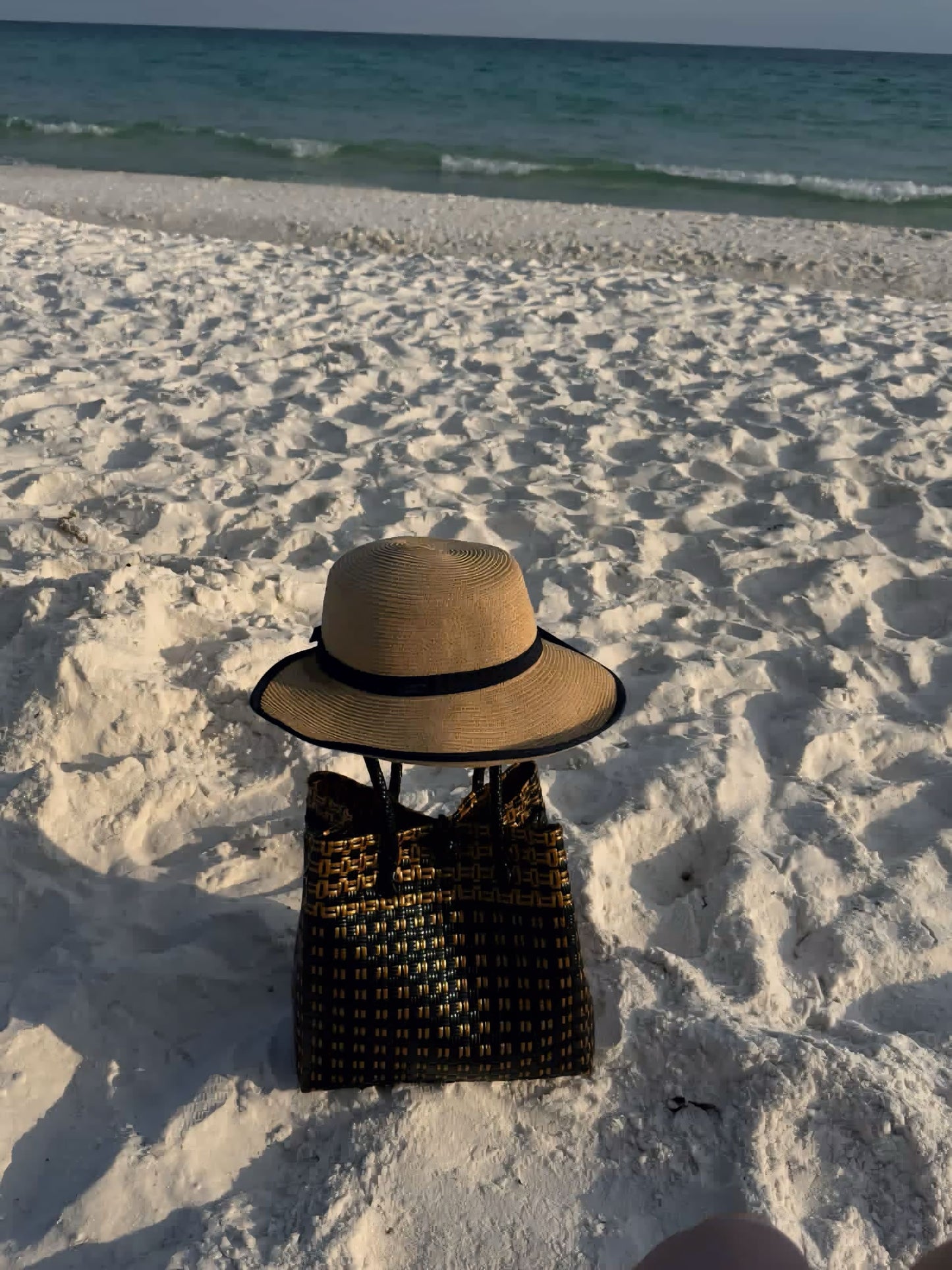Woven bag and straw hat on a sandy beach with ocean in the background